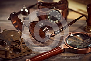 Steampunk still life - old vintage objects on a wooden background. Leather wrist watch, dark glasses, old tube lamps, magnifying g