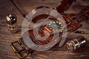 Steampunk still life - old vintage objects on a wooden background. Leather wrist watch, dark glasses, old tube lamps, magnifying g