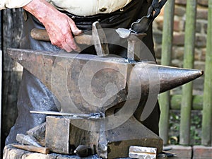Steel anvil, on top of which lies a hot workpiece, the hand of the blacksmith processes a workpiece with the aid of a hammer