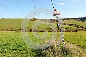 Steel cables at power electricity pylon with red warning triangles with exclamation mark - danger, high voltage, small