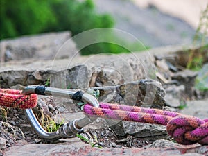 Steel carabine hook with a climbing-rope on rock background. Closeup.