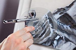 Steel chrome airbrush device in human hand, painting with aerograph, close-up view