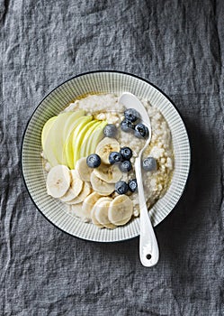 Steel-cut oats breakfast porridge with apple, banana, blueberry and honey on a grey background