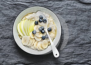 Steel-cut oats breakfast porridge with apple, banana, blueberry and honey on a grey background