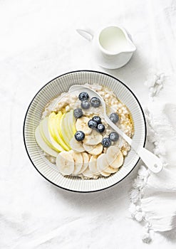 Steel-cut oats breakfast porridge with apple, banana, blueberry and honey on a light background. Vegetarian healthy food