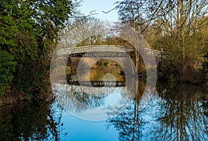 The Steel footbridge over the River Stort, or Lee & Stort Navigation, on a summers day with local trees reflecting in the still wa