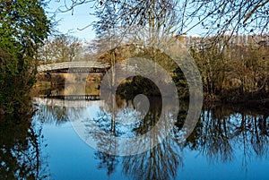 The Steel footbridge over the River Stort, or Lee & Stort Navigation, on a summers day with local trees reflecting in the still wa