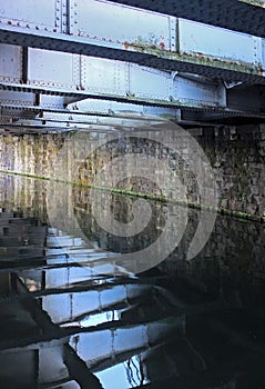 Steel girders reflected reflected in the water of a dark canal under a bridge