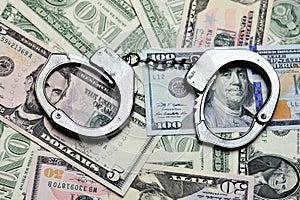 Steel handcuffs above US dollar banknotes, tax evasion concept