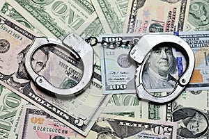Steel handcuffs above US dollar banknotes, tax evasion concept photo