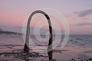 Steel hinges from reinforcement stick out of the water on the old pier. Dawn. Mainly cloudy. Coast