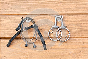 Steel horse snaffle-bit and spurs hanging on wooden background