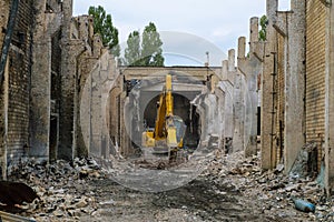 Steel hydraulic attachment pliers on excavator grappling construction debris in collapsed industrial building