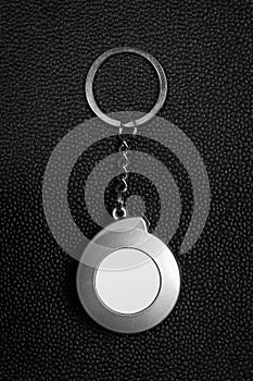 Steel key chain on dark leather background. Blank keyring in measuring tape concept