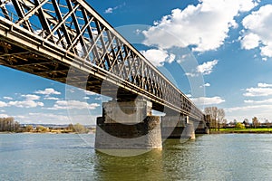 Steel, lattice structure of a railway bridge over a river with a background of blue sky with white clouds in western Germany.