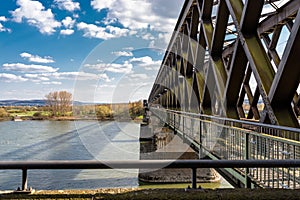 Steel, lattice structure of a railway bridge over a river with a background of blue sky with white clouds in western Germany.