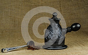 A steel measuring spoon with roasted coffee beans and a made of black clay Ñoffeepot on a coarse canvas background
