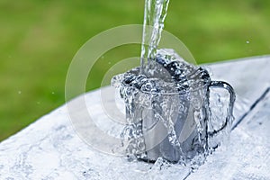 A steel mug with water and sprays on a white wooden table on nature background