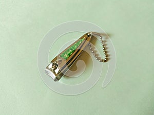 Steel nail clipper isolated on mint color background. Green design on top and ball chain for hang.