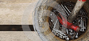 steel nail construction tool in rusty iron bucket. High angle view of various equipment in bucket on wooden boards floor. top view