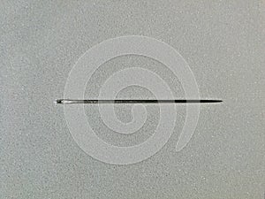 Steel needle for hand sewing, placed on a gray background