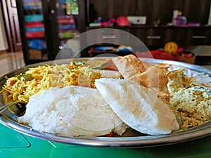 A steel plate containing Indian breakfast items like Idlis, Poori, Vermicelli and Chutney