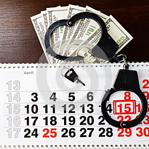 Steel police handcuffs, dollars money and April 15 on calendar o