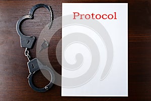 Steel police handcuffs and empty protocol list lying on wooden t