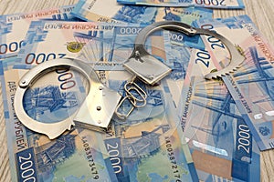 Steel police handcuffs lying on the background of dollars with folded stack of banknotes of russian roubles .