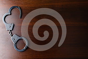 Steel police handcuffs lying on the wooden table, top view, copy