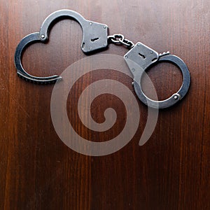 Steel police handcuffs lying on the wooden table, top view, copy