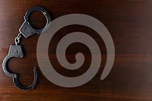 Steel police handcuffs lying on the wooden table, top view, copy