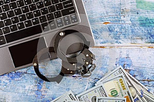 Steel police handcuffs on a pile of one hundred dollar bills with computer keyboard, technology cyber crime internet