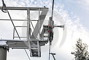 Steel ropes over wheels in mechanism on top of ski chair lift support pillar, bright sky background