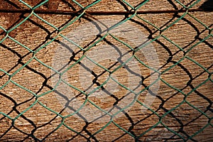 Steel rusty metal mesh on wooden background. Mesh pattern on the background of an old wooden wall. Green chain-link fence