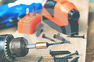 A steel screw is placed on an electric drill on a wooden board background. The concept of tools and repair work. Steel screws
