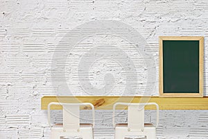 Steel Stools with Wooden Shelf and Blank Black Chalkboard on White Brick Wall Background