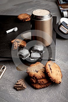 Steel thermo coffee bottle on gray concrete background with macaroons and smartphone. Tinting