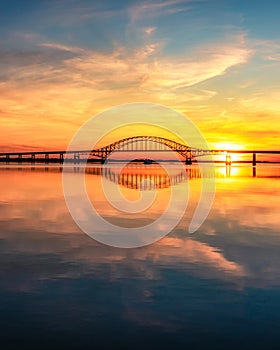 Steel tied arch bridge spanning a bay with crystal clear reflections in the water at sunset. Fire Island New York