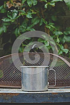 A steel tin coffee mug on the old garden table in the vines