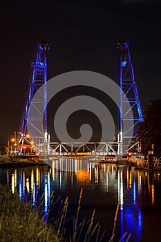 Steel vertical lift bridge in Waddinxveen, Netherlands over the canal Gouwe is illuminated by blue light beams at night.