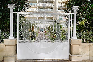 Steel white metal gate with forged pattern and brick fence on sidewalk on street