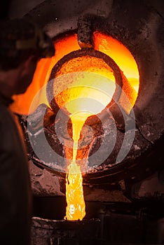 Steel worker in protective clothing raking furnace in an industrial foundry