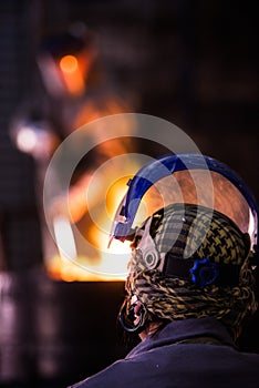 Steel worker in protective clothing raking furnace in an industrial foundry