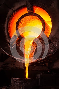 Steel worker in protective clothing raking furnace in an industrial foundry