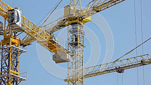 Steel yellow construction cranes over blue sky background.