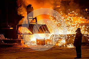 Steelworker near a blast furnace with sparks.