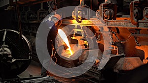 A steelworker pours molten metal from a crucible into molds in the steel industry, a conveyor moves.