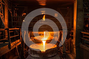 Steelworker at work near arc furnace and pouring liquid metal