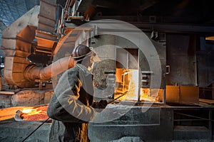 Steelworker at work near arc furnace and pouring liquid metal.